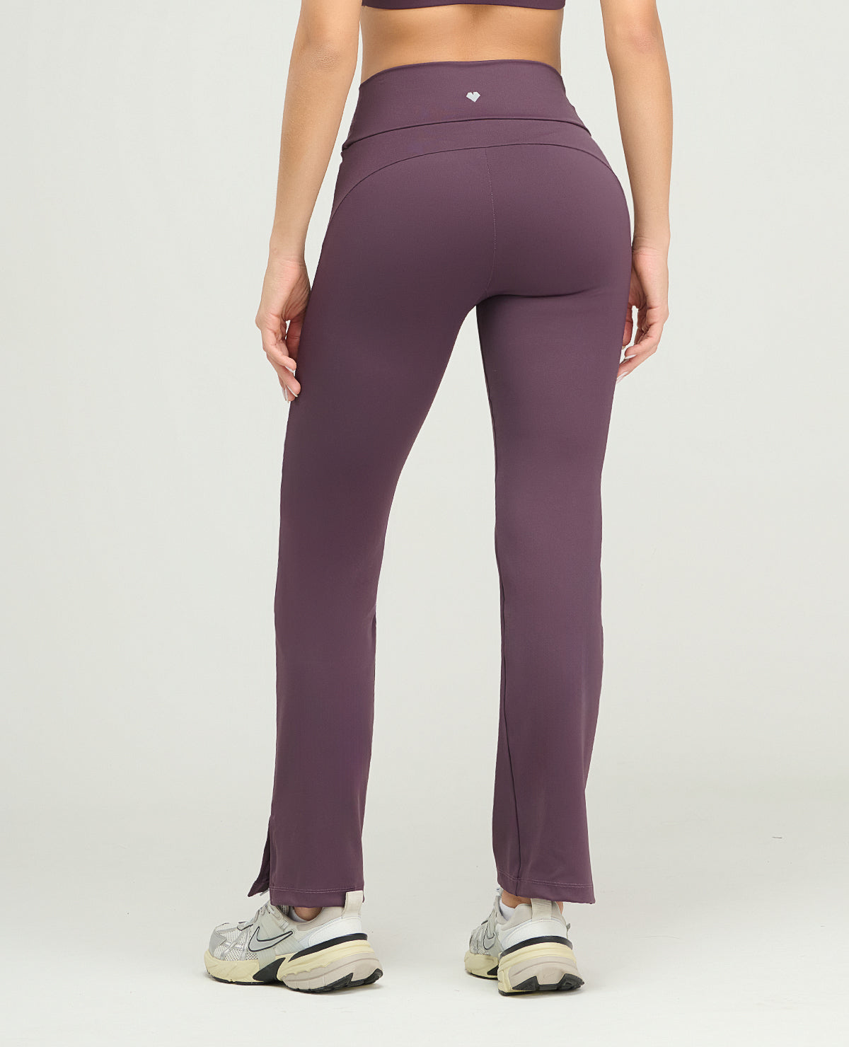 Vista posterior de pantalón deportivo tipo leggings morado con silueta ajustada, pretina alta y bota recta con abertura.