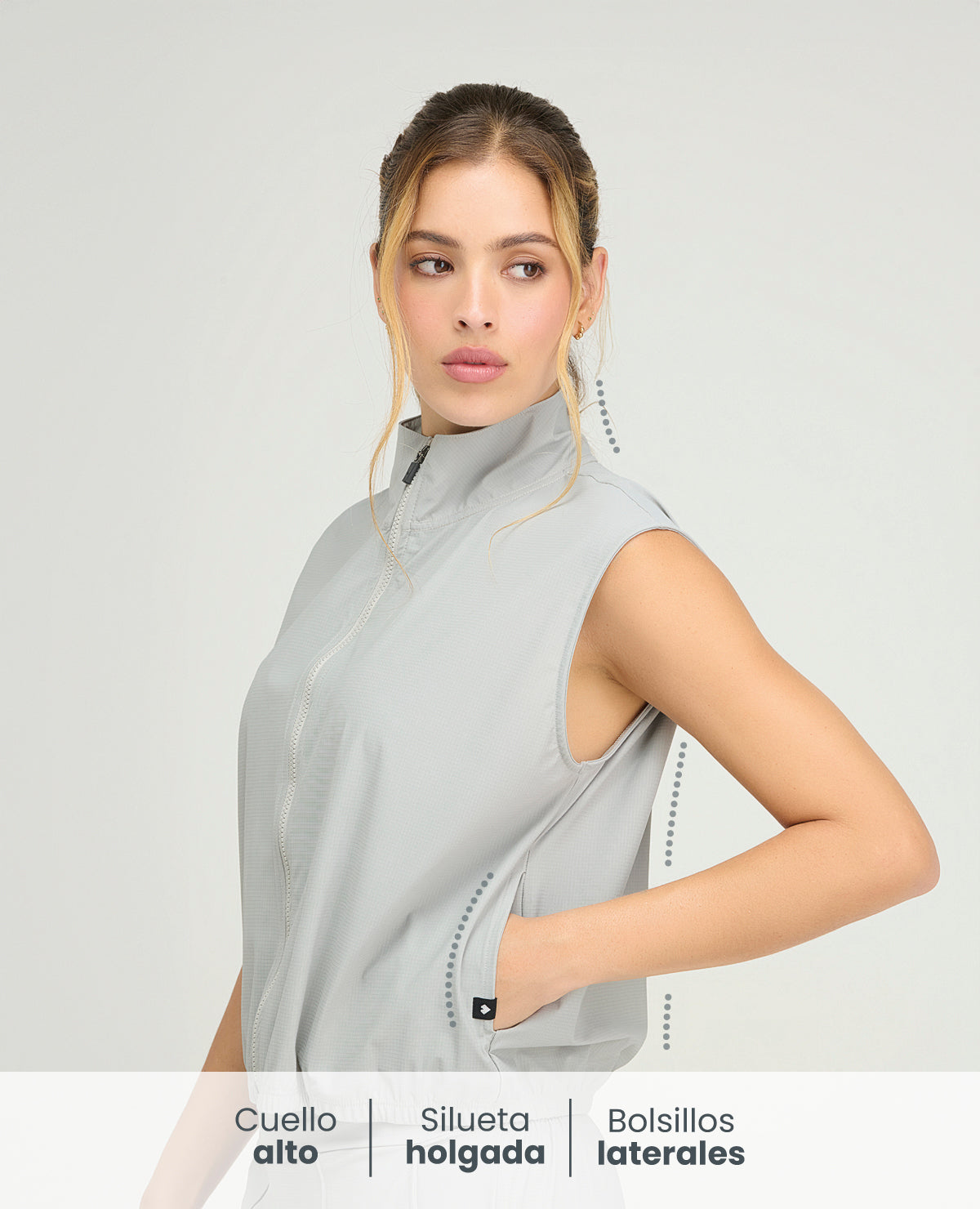 Chaleco deportivo gris para mujer con cuello alto, cremallera frontal y bolsillos laterales de silueta holgada.