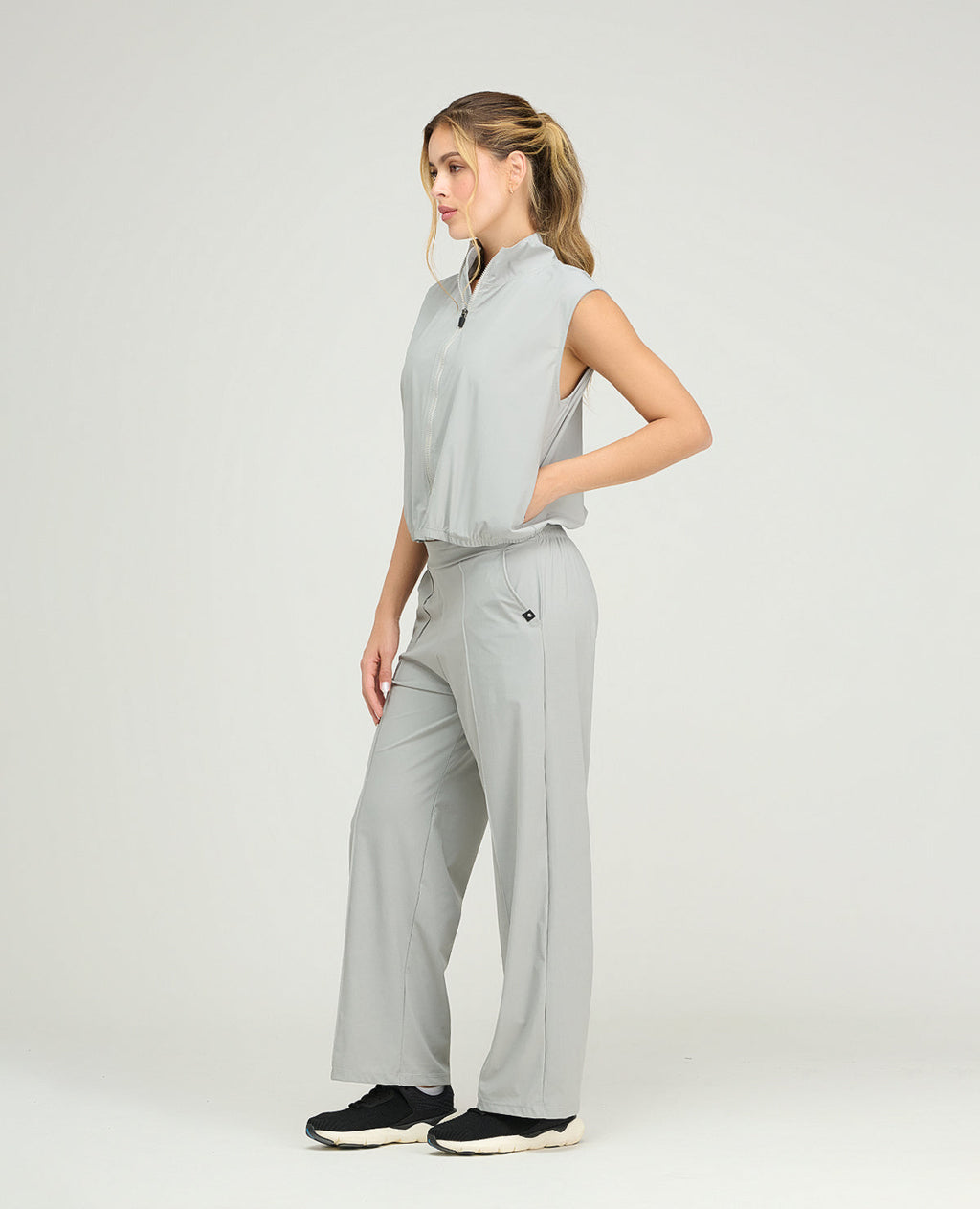 Chaleco deportivo gris para mujer con cuello alto, cremallera frontal y bolsillos, ideal para gimnasio y running.