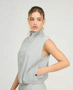 Mujer usando chaleco deportivo gris con cuello alto, cremallera frontal y bolsillos, ideal para gimnasio y running.