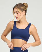 Modelo usando top deportivo azul con escote cuadrado, cargaderas anchas y tecnología seamless sin costuras.