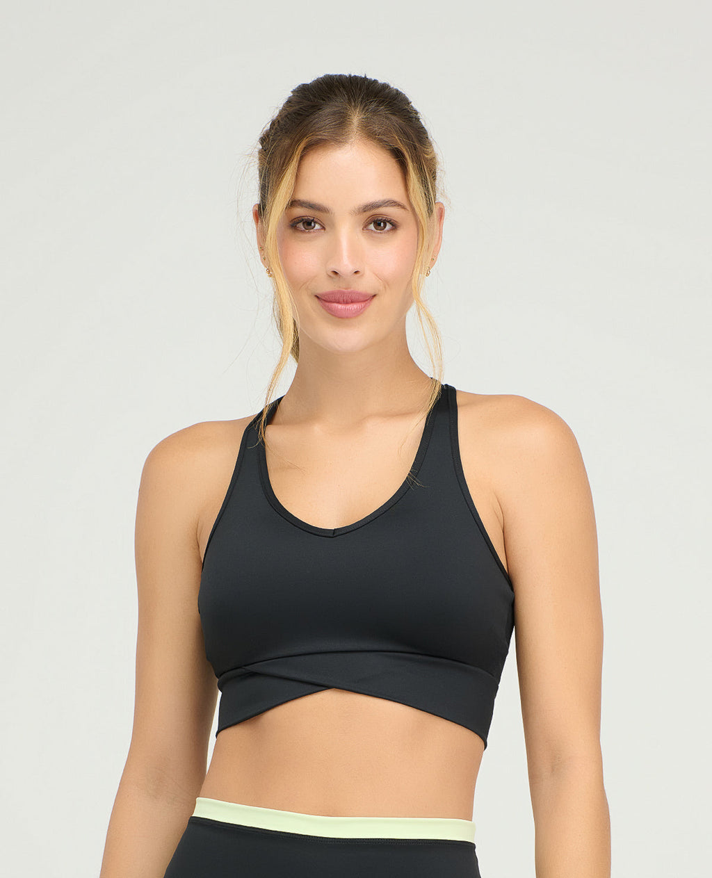 Top deportivo negro ajustado con cargaderas anchas y base estructurada cruzada frontal sobre fondo gris claro.