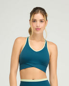 Top deportivo azul petróleo para mujer, silueta ajustada con cargaderas anchas y base cruzada de soporte.