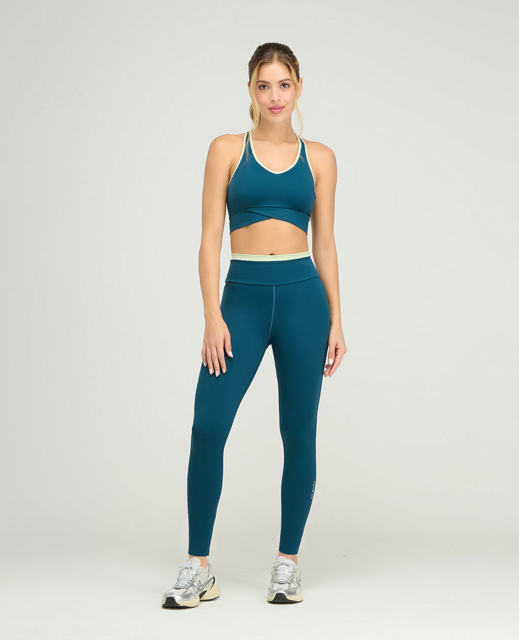 Top deportivo azul cerceta de silueta ajustada con cargaderas anchas y base cruzada sobre leggins a juego.