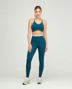 Top deportivo azul cerceta de silueta ajustada con cargaderas anchas y base cruzada sobre leggins a juego.