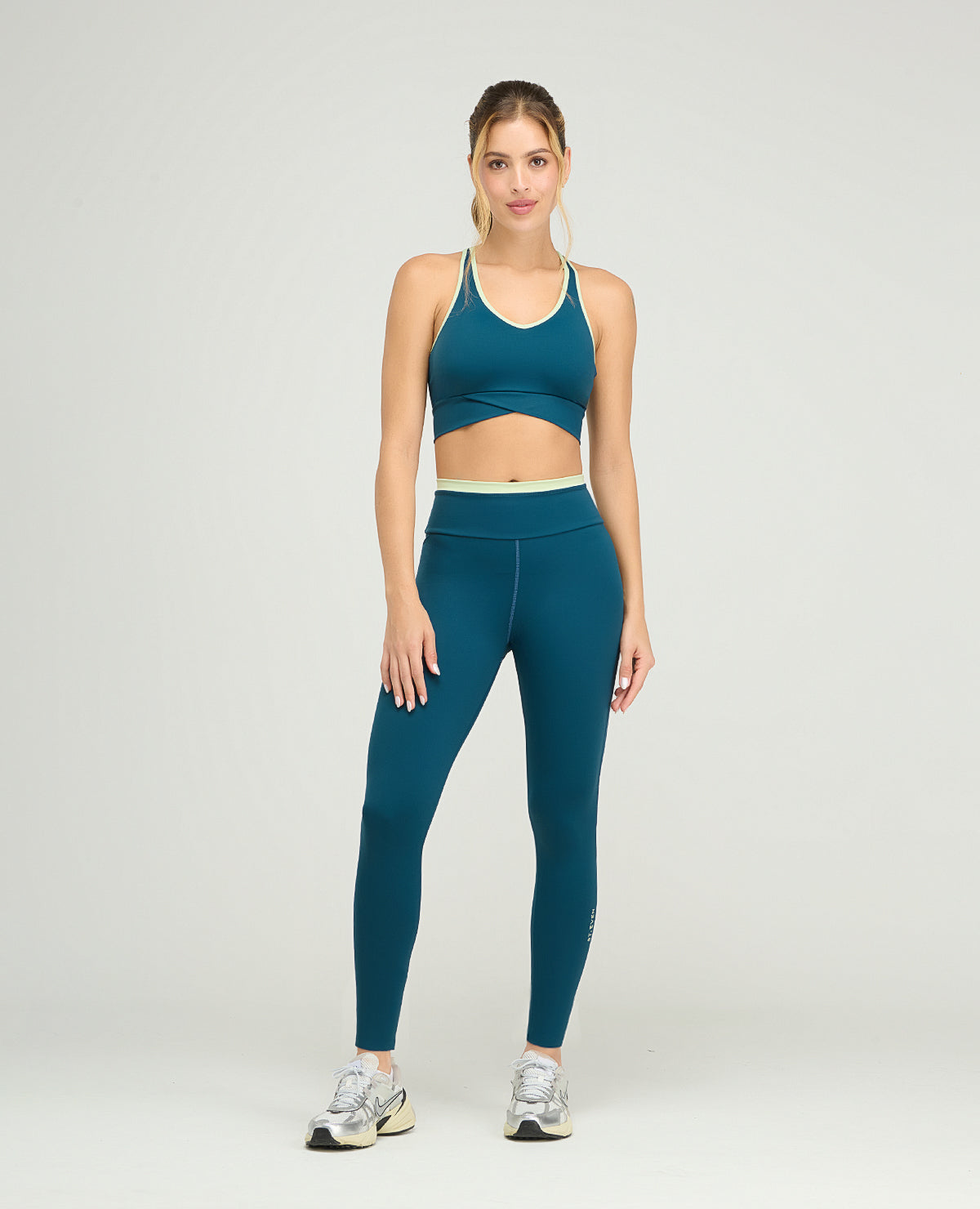 Top deportivo azul cerceta de silueta ajustada con cargaderas anchas y base cruzada sobre leggins a juego.