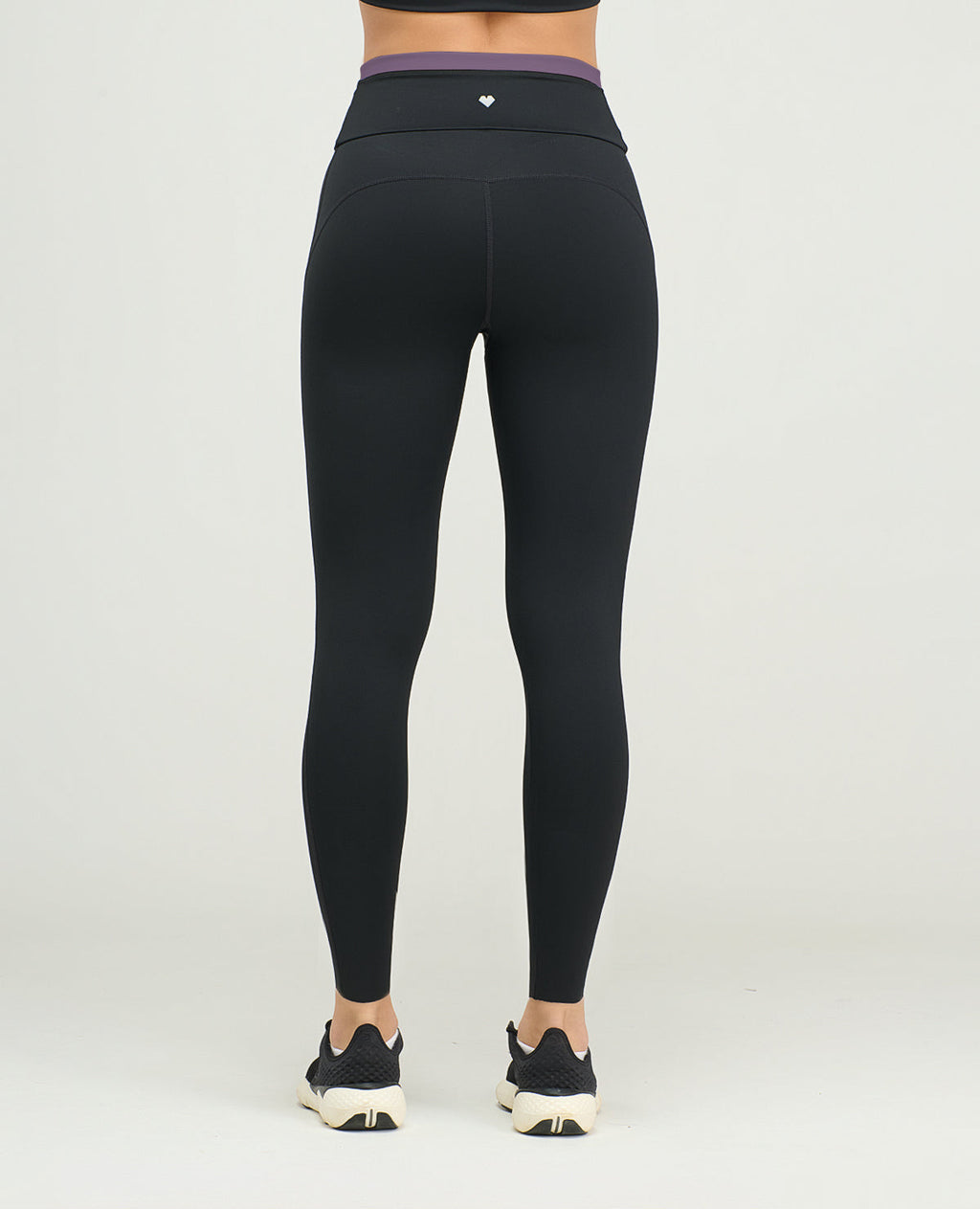 Vista posterior de leggins deportivos para mujer en negro, silueta ajustada de talle alto con vivo morado en cintura.