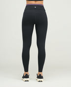 Vista posterior de leggins deportivos para mujer en negro, silueta ajustada de talle alto con vivo morado en cintura.