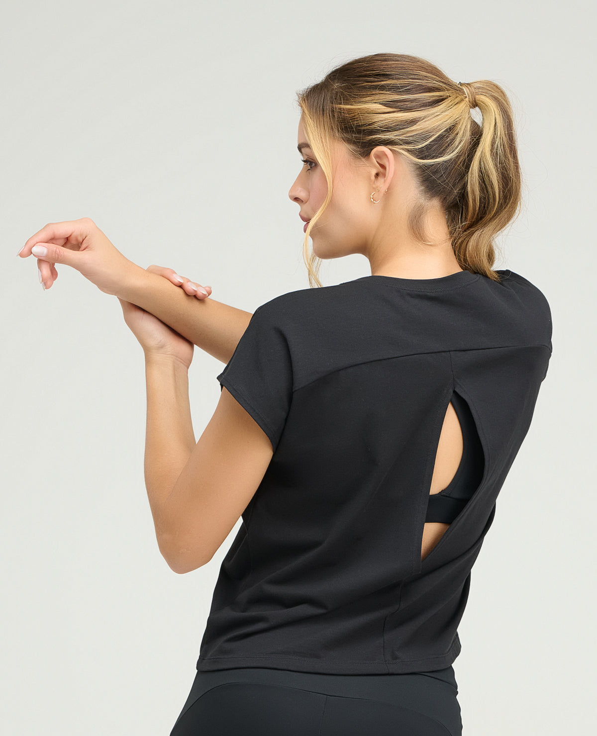 Vista posterior de camiseta deportiva negra para mujer con abertura en espalda, silueta holgada y manga rodada.