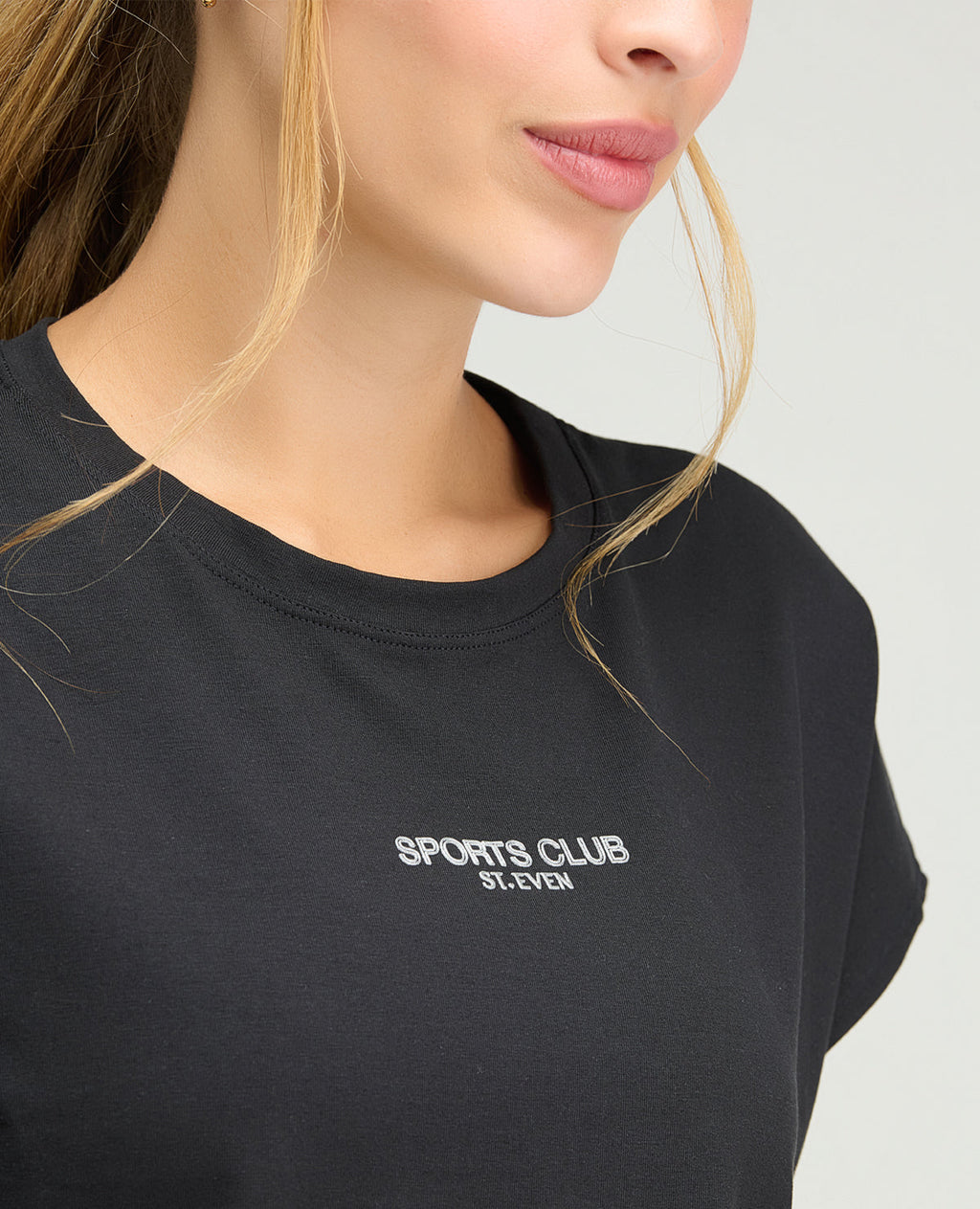 Primer plano de camiseta deportiva negra para mujer con cuello redondo y logo Sports Club St. Even.
