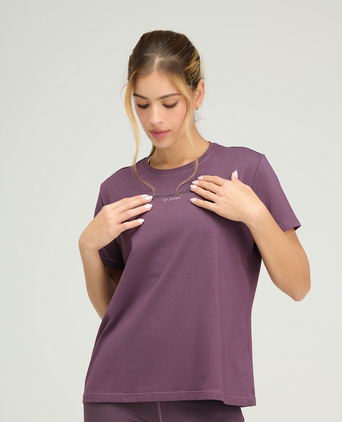 Camiseta deportiva color berenjena para mujer con silueta holgada, cuello redondo y detalle reflectivo frontal.
